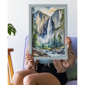 May include: A framed watercolor painting of a waterfall cascading down a mountainside. The painting features a blue sky, green trees, and a river flowing through the valley.