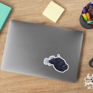 May include: A black and white sticker of a anglerfish with a bioluminescent lure on a gray laptop.