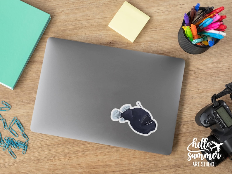 May include: A black and white sticker of a anglerfish with a bioluminescent lure on a gray laptop.