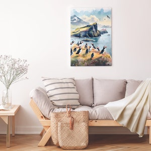 May include: A watercolor painting of a cliffside with a group of puffins standing on the edge. The painting is framed and hanging on a white wall above a light gray couch.