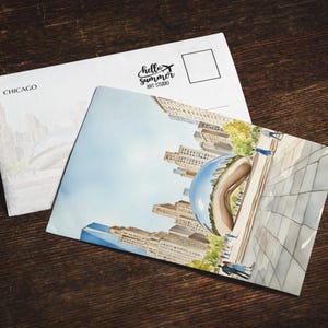 May include: Watercolor postcard featuring a Chicago cityscape with the iconic Cloud Gate sculpture. The postcard is paired with a white envelope, both resting on a dark wooden surface. The envelope has the word "Chicago" and the "hello summer ART STUDIO" logo.