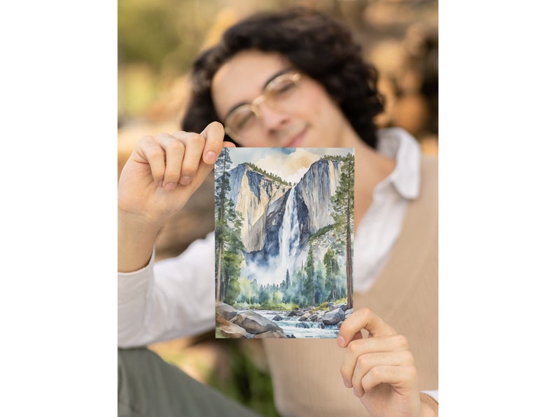 May include: A watercolor painting of Yosemite Falls in California. The painting depicts the waterfall cascading down a rocky cliff face, surrounded by lush green trees. The water is a light blue color, and the sky is a pale blue with hints of orange and yellow.