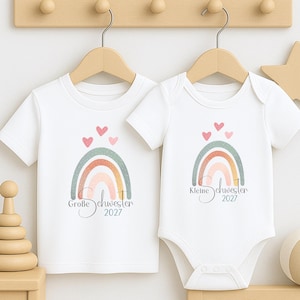 Könnte beinhalten: Ein weißes T-Shirt mit kurzen Ärmeln und ein weißer Body mit kurzen Ärmeln, jeweils mit einem Regenbogen-Aufdruck und drei kleinen Herzen darüber. Das T-Shirt zeigt den Text Große Schwester 2027 und der Body zeigt Kleine Schwester 2027.