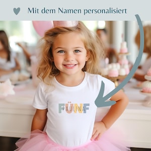 May include: A white short-sleeved t-shirt featuring the word F&Uuml;NF in muted pastel block letters with the name PAULINA printed in black across the center. The text Mit dem Namen personalisiert appears at the top with a heart icon.