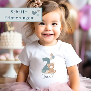 Peut inclure: Un t-shirt blanc &agrave; manches courtes orn&eacute; d'un motif repr&eacute;sentant le chiffre deux, un ours en peluche marron, un cadeau et trois petits ballons. Le pr&eacute;nom Linea est inscrit sous le motif. Un encadr&eacute; affiche les mots Schaffe Erinnerungen.