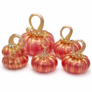 May include: A collection of five glass pumpkins in varying sizes. The pumpkins are a vibrant red with gold accents, featuring ribbed detailing and curly gold stems. The decorative gourds are ideal for fall decor.