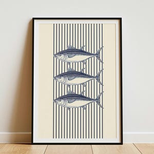 May include: A framed wall art print featuring three stacked illustrations of tuna fish in dark blue ink. The fish are centered over a background of vertical dark blue stripes on a cream-colored field, all enclosed within a thin black frame.