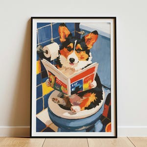 May include: A framed wall art print featuring a black, white, and tan Corgi sitting on a blue toilet in a tiled bathroom. The dog is holding an open, colorful magazine with red, yellow, and blue pages. A roll of white toilet paper is visible.