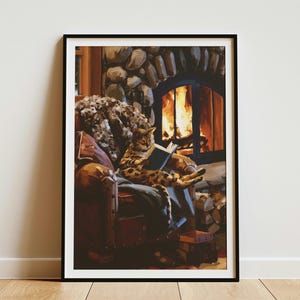May include: A framed wall art print depicting a spotted cat sitting in a brown leather armchair, reading an open book. The scene features a stone fireplace with a glowing fire in the background, a textured throw blanket, and a stack of firewood.