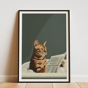 May include: A framed art print featuring a brown tabby cat in a bathtub, reading a newspaper. The cat is the focal point, with a dark green background and a white bathtub. The print has a black frame and is displayed on a white wall.