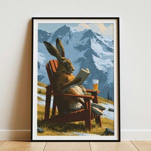 May include: A framed art print depicting a brown rabbit sitting in a red wooden Adirondack chair on a grassy hillside. The rabbit is reading an open book and has a glass of beer nearby. In the background, there are snow-capped mountain peaks.
