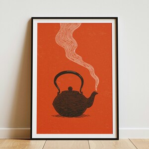 Könnte beinhalten: Ein gerahmter Wandkunstdruck mit einer dunkel anthrazitfarbenen gusseisernen Teekanne, die auf einem leuchtend orangefarbenen Hintergrund zentriert ist. Die Teekanne hat einen geschwungenen Griff und einen Ausguss mit einer dünnen, weißen, welligen Linie.