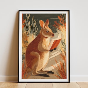 May include: Framed art print featuring a wallaby reading a book. The wallaby is depicted in warm brown tones, holding an open book with orange pages. The background includes tall, orange-hued grasses and a dark green backdrop, creating a nature-inspired scene.