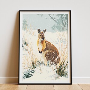 May include: Framed art print featuring a wallaby in a snowy landscape. The wallaby has brown and tan fur, with a white belly. The artwork is set in a snowy field with tall grass and a tree in the background. The print is in a black frame.