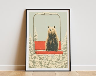 May include: A framed art print featuring a bear sitting on a red ski lift chair. The bear is brown with a light-colored face, set against a snowy forest backdrop. The print has a vintage, illustrated style.