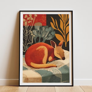 May include: Framed art print featuring a sleeping kangaroo. The kangaroo is depicted in shades of orange and brown, resting on a checkered blanket. The background includes stylized botanical elements in red, black, and gold. The artwork is framed in a black border.