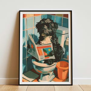 May include: A framed wall art print featuring a black, curly-haired dog sitting on a white toilet in a bathroom with blue tiled walls. The dog is holding an open newspaper with orange and green graphics. An orange bucket sits on the floor nearby.