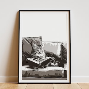 May include: Black and white framed art print of a cat reading a book while lounging on a sofa. The cat is the focal point, with detailed fur and focused eyes. The sofa and pillows are in shades of gray.