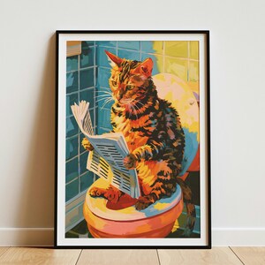May include: A framed wall art print featuring a brown tabby cat sitting on a toilet and reading a newspaper. The cat is positioned in front of blue tiled walls, with the toilet seat and lid visible in shades of yellow, orange, and red.