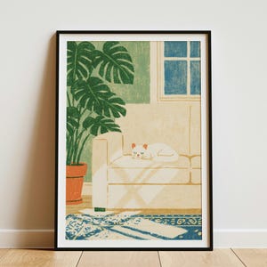 May include: A framed art print featuring a white cat sleeping on a beige sofa next to a large green monstera plant in a terracotta pot. A blue window is visible in the background, and a blue and white patterned rug lies on the floor below.