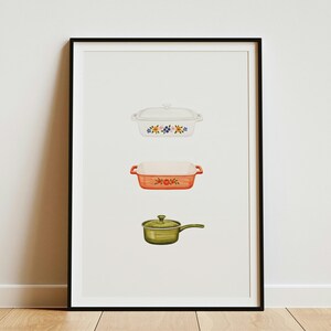 May include: A framed vertical print featuring three kitchen items stacked vertically: a white rectangular casserole dish with a floral pattern, an orange rectangular baking dish with a floral design, and a green saucepan with a lid.
