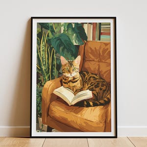 May include: A framed art print depicts a Bengal cat lounging on a brown armchair, engrossed in a book. The cat has a distinctive spotted coat and is positioned in front of lush green foliage. The artwork is set against a neutral wall.