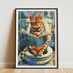 May include: A framed wall art print featuring a tabby cat with green eyes sitting on a white toilet while reading a blue newspaper. The background shows blue tiled walls and a colorful tiled floor, all rendered in a painterly, graphic style.