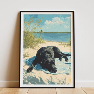 May include: Framed art print of a black Labrador Retriever resting on a blue towel at the beach. The artwork features a sunny day with blue skies, water, and sand. The dog is the focal point of the image.