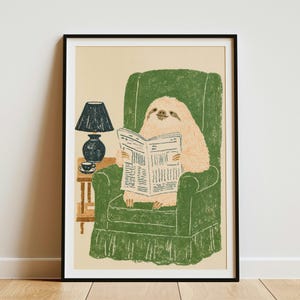 May include: A framed print featuring a light brown sloth sitting in a textured green armchair, reading a newspaper. Beside the chair is a small wooden side table holding a dark blue lamp and a small cup, all set against a light beige background.