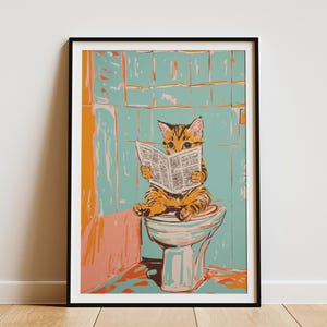 May include: Framed art print featuring a tabby cat sitting on a toilet, engrossed in reading a newspaper. The artwork has a whimsical style with a color palette of orange, teal, and white. The background is a stylized bathroom setting.