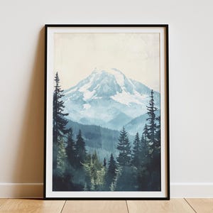 May include: Framed art print featuring a mountain landscape. The artwork depicts a snow-capped mountain in the background, with layers of blue-toned mountains and a forest of evergreen trees in the foreground. The print is encased in a black frame.