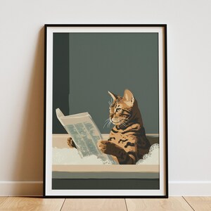 May include: A framed wall art print featuring a brown tabby cat with dark stripes sitting in a bathtub filled with white bubbles. The cat is holding an open newspaper with visible text, looking toward the left side of the frame against a dark green background.