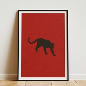 May include: A rectangular wall art print featuring a solid black silhouette of a prowling panther centered against a textured, deep red background. The artwork is enclosed within a thin black frame, presenting a high-contrast graphic design.
