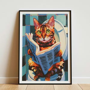 May include: A framed wall art print featuring a colorful painting of a tabby cat with green eyes sitting on a white toilet while reading a blue newspaper. The background consists of a grid of blue and black square tiles in a bathroom setting.