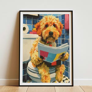 May include: A framed wall art print featuring a golden-coloured dog sitting on a white toilet in a blue-tiled bathroom. The dog is holding an open newspaper with colourful graphic blocks. The scene includes a toilet paper roll and a pink towel.