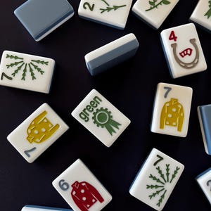 May include: A collection of white and blue Mahjong tiles with various symbols and numbers. The tiles feature green, red, and yellow designs, including a horseshoe, a rose, and a ribbon. The word "green" is printed on one tile.
