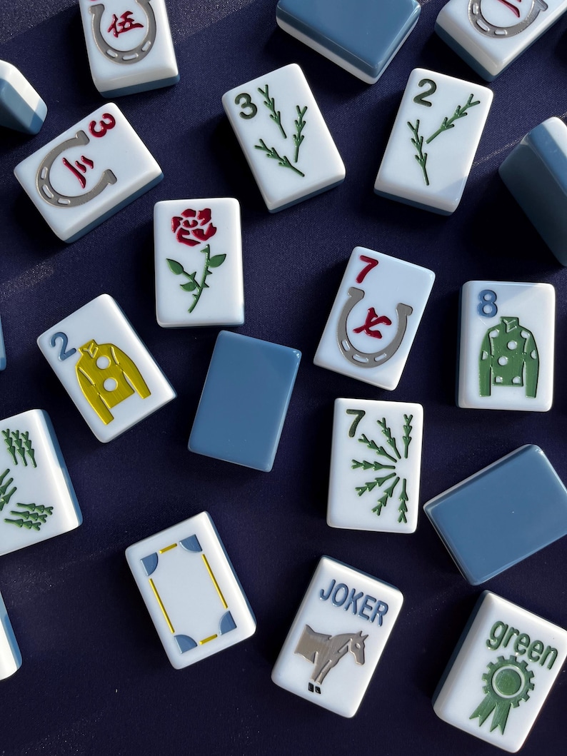 May include: A collection of white and blue Mahjong tiles with various symbols and numbers. The tiles feature images of a rose, a horseshoe, and a horse. Some tiles have the word "JOKER" and "green" printed on them.