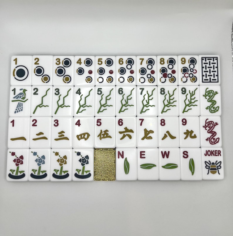 May include: A set of white Mahjong tiles with black, green, red, and gold markings. The tiles feature various symbols, numbers, and Chinese characters. The set includes tiles with the words "NEWS" and "JOKER".