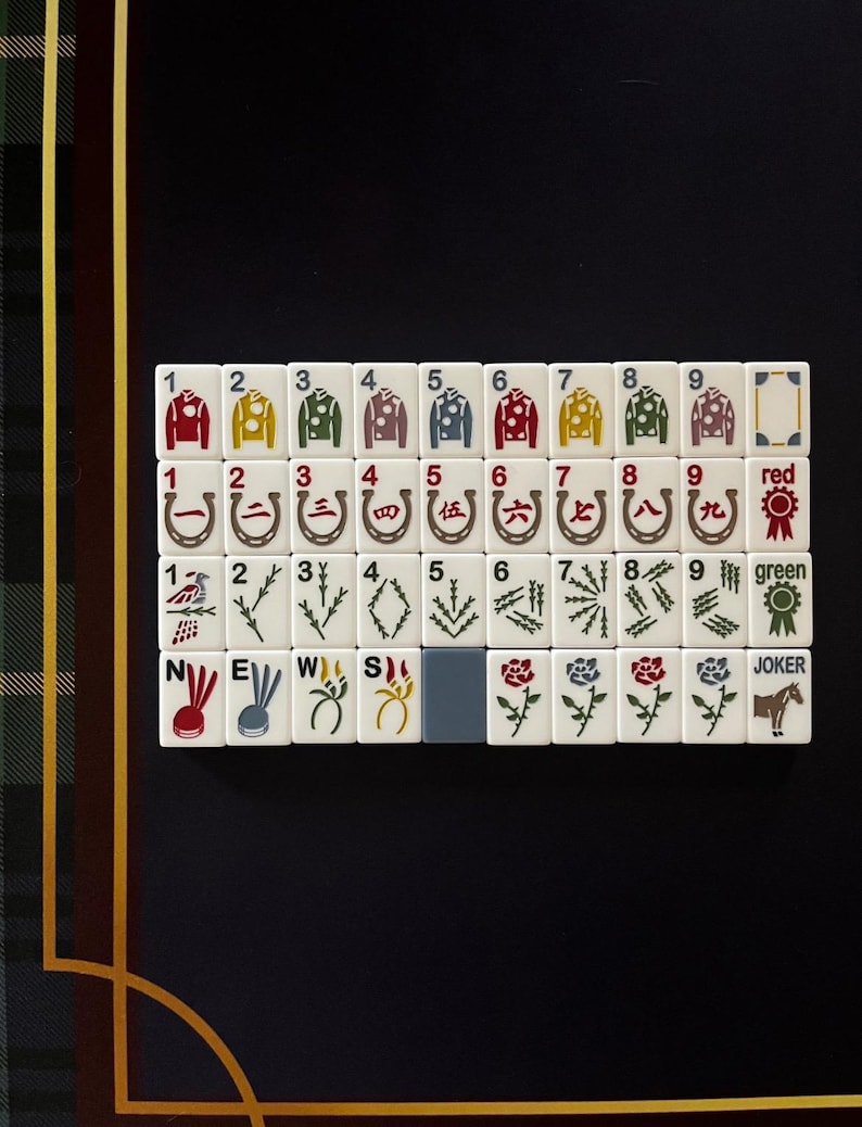 May include: A set of white Mahjong tiles arranged on a black surface. The tiles feature various symbols, numbers, and characters, including horse racing silks, horseshoe shapes, and Chinese characters. The set includes red and green tiles.