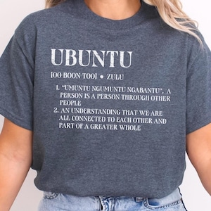 May include: A dark heather grey t-shirt with white text that reads "UBUNTU 100 BOON TOOL ZULU 1. "UMUNTU NGUMUNTU NGABANTU", A PERSON IS A PERSON THROUGH OTHER PEOPLE 2. AN UNDERSTANDING THAT WE ARE ALL CONNECTED TO EACH OTHER AND PART OF A GREATER WHOLE"