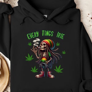 May include: Black hoodie featuring a skeleton with dreadlocks, a colorful hat, and a cigarette. The skeleton is surrounded by marijuana leaves and the text "EVERY TINGS IRIE" in green. The hoodie has a drawstring hood.
