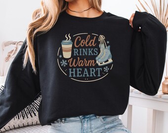 以下が含まれることがあります： コーヒーカップ、スケート靴、そして「Cold Rinks Warm Heart」の文字が描かれた円形のグラフィックが特徴の黒いスウェットシャツ。デザインには雪の結晶が含まれており、茶色、青、白の色合いです。