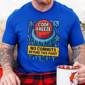 Puede incluir: Una camiseta azul real con un diseño gráfico que presenta un botón rojo con la etiqueta "CODE FREEZE" rodeado de hielo y copos de nieve. Debajo, un letrero amarillo dice "NO COMMITS BEYOND THIS POINT."