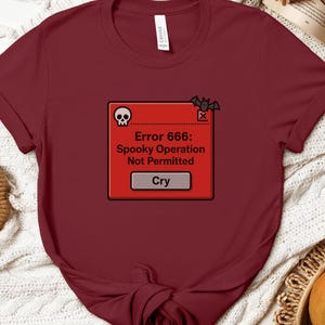 May include: Burgundy t-shirt with a red error message graphic. The graphic includes a skull, bat, and the text "Error 666: Spooky Operation Not Permitted" and the word "Cry".