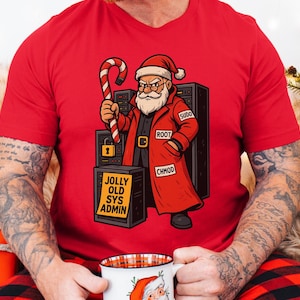 May include: Red t-shirt with a cartoon Santa Claus holding a candy cane. Santa is depicted with a stern expression, wearing a red coat with the words "Sudo", "Root", and "Chmod". The shirt also has the text "Jolly Old Sys Admin".