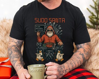Puede incluir: Camiseta negra con un gráfico de Papá Noel con una sudadera roja, gafas de sol y barba blanca, sentado en un trono de unidades USB. El texto "SUDO SANTA" está encima del gráfico, y un letrero dice "$ sudo give-gifts --recursive".