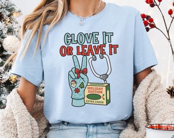 May include: Light blue t-shirt with the text "GLOVE IT OR LEAVE IT" in green and red. The graphic includes a peace sign hand wearing a medical glove, a stethoscope, and a box labeled "HOLIDAY EDITION EXTRA CHEER".