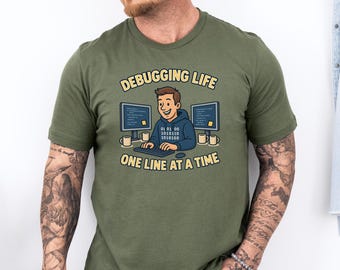 May include: Olive green t-shirt with the text "Debugging Life One Line at a Time." The graphic features a cartoon programmer at a computer. The programmer is wearing a blue hoodie and is sitting in front of two computer monitors.