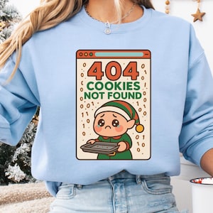 May include: Pale blue sweatshirt with a graphic of a dejected elf holding a baking tray. The graphic is within a computer window displaying "404 COOKIES NOT FOUND". The elf wears a green and red outfit and a pointed hat.