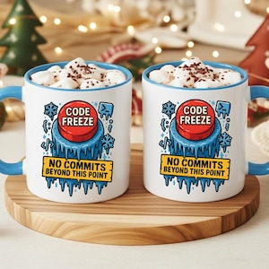 Könnte beinhalten: Zwei weiße Tassen mit blauen Griffen und Rändern, jede mit einer "Code Freeze"-Grafik mit einem roten Knopf und dem Text "No Commits Beyond This Point". Die Tassen sind mit Marshmallows und Kakao gefüllt.